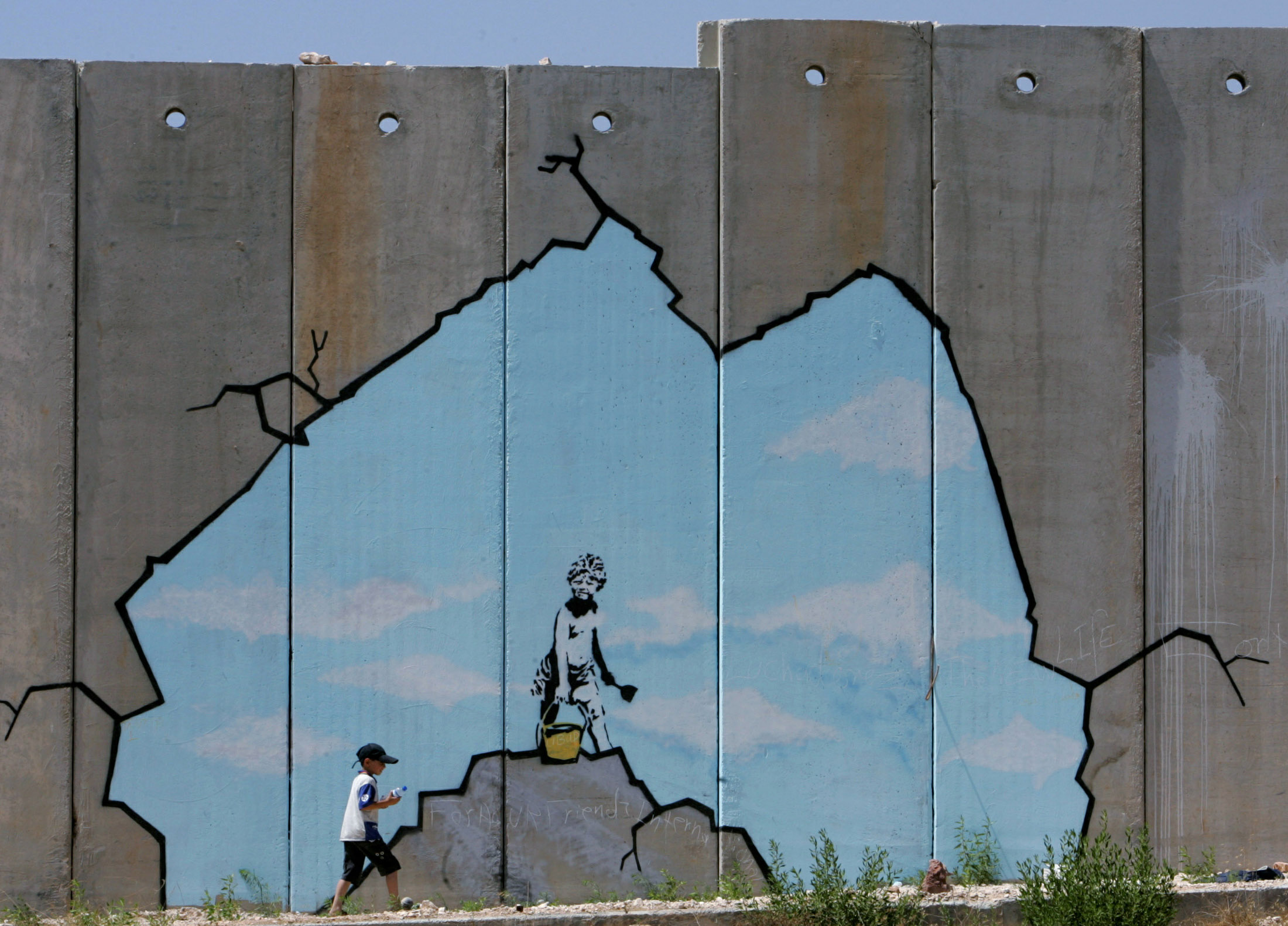 A Palestinian boy walks past a drawing by British graffiti artist Banksy, along part of the controversial Israeli barrier near the Kalandia checkpoint in the West Bank August 10, 2005. Photo by Ammar Awad/REUTERS.