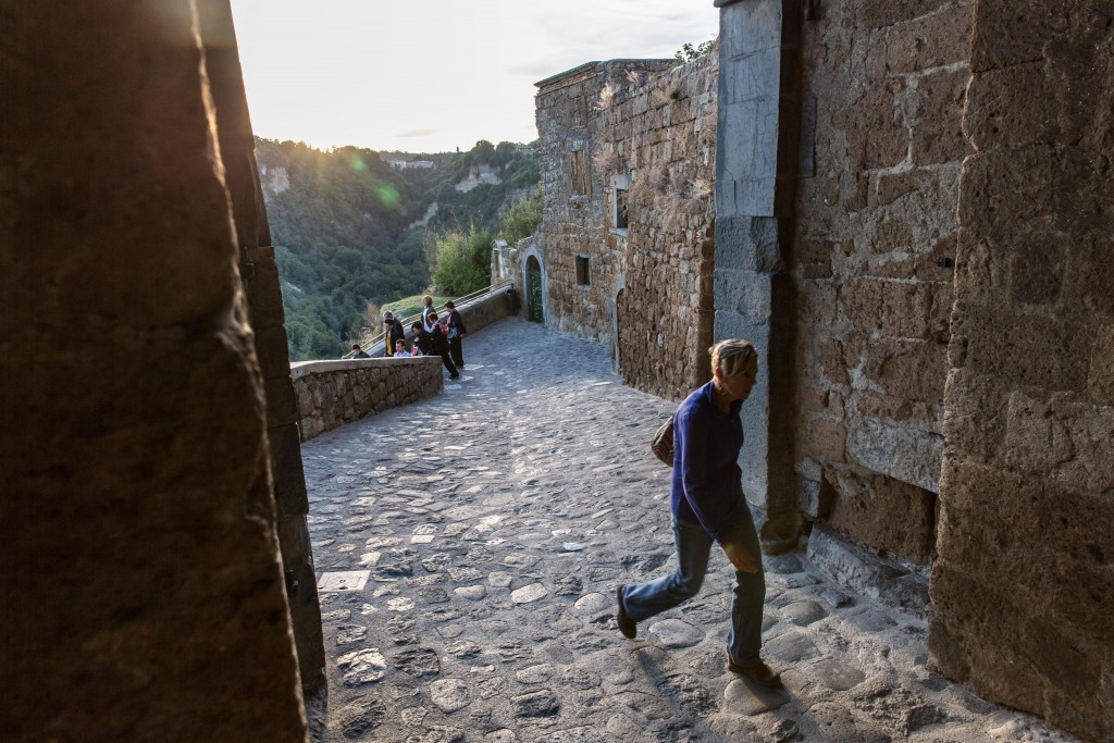 Sunlight fades as a woman enters Civita di Bagnorio from the footbridge as others leave for the day. Photo by Frank Carlson