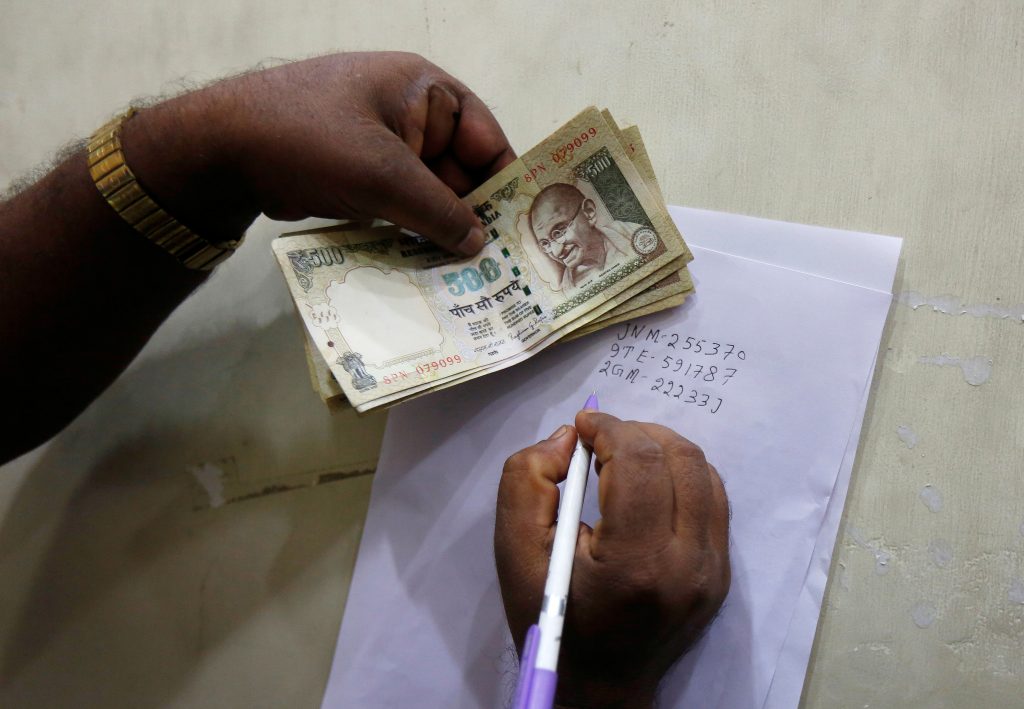 A man writes the serial numbers of 500 Indian rupee banknotes on the back of a form before depositing them in a bank in Kolkata, India. Photo by Rupak De Chowdhuri/Reuters