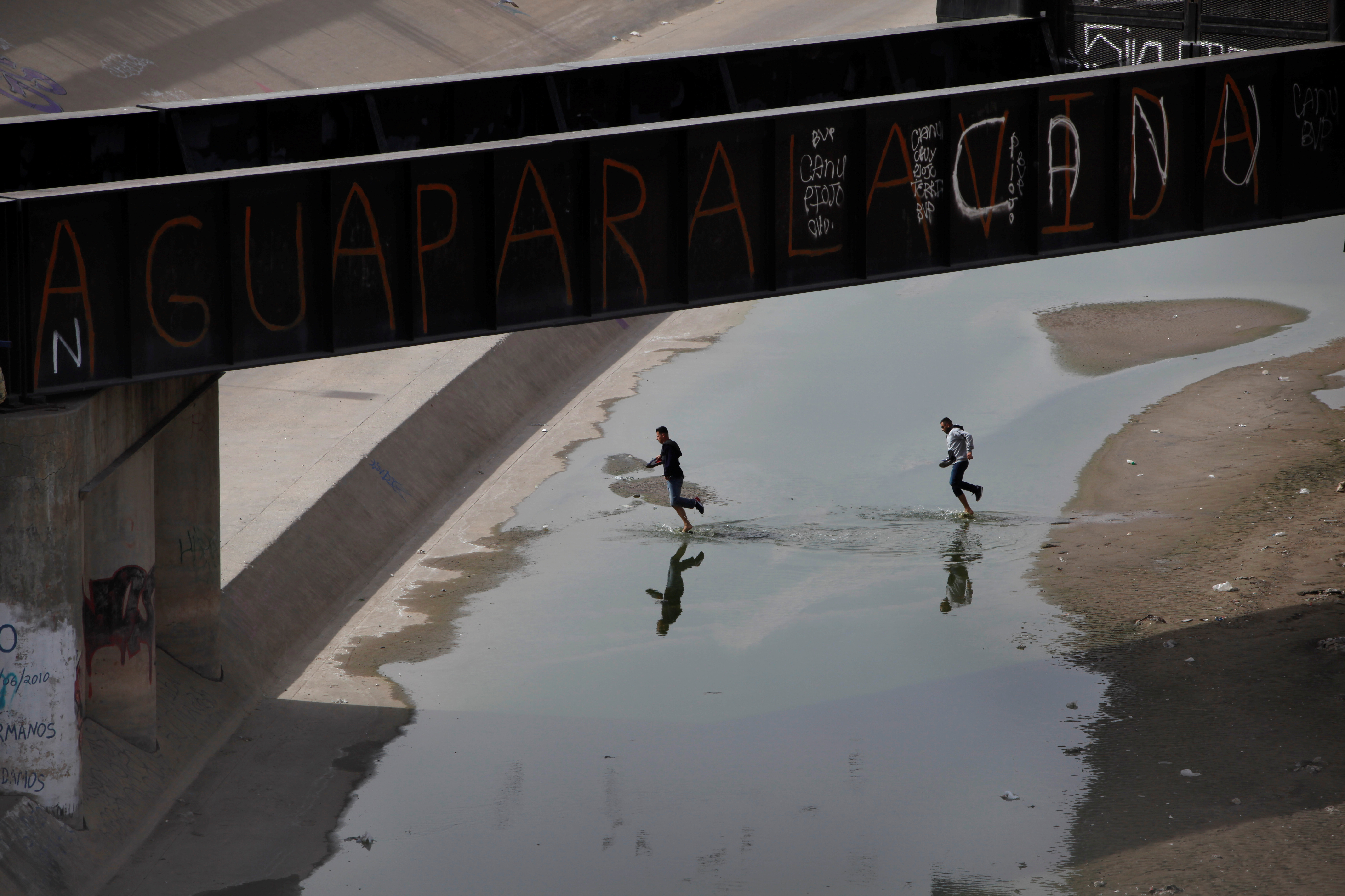 Men run along the banks of the Rio Bravo and the natural border between the U.S. and Mexico, in Ciudad Juarez, Mexico. The writing on the pedestrian bridge reads "water for life." Photo by Jose Luis Gonzalez/Reuters