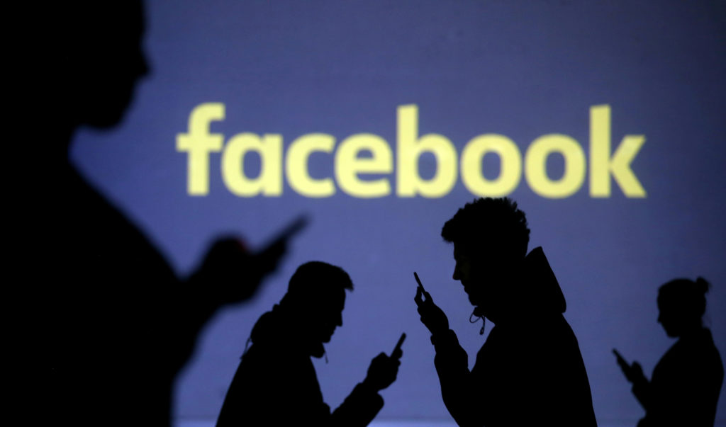 Silhouettes of mobile users are seen next to a screen projection of the Facebook logo in this picture illustration. File photo by Dado Ruvic/Illustration/Reuters