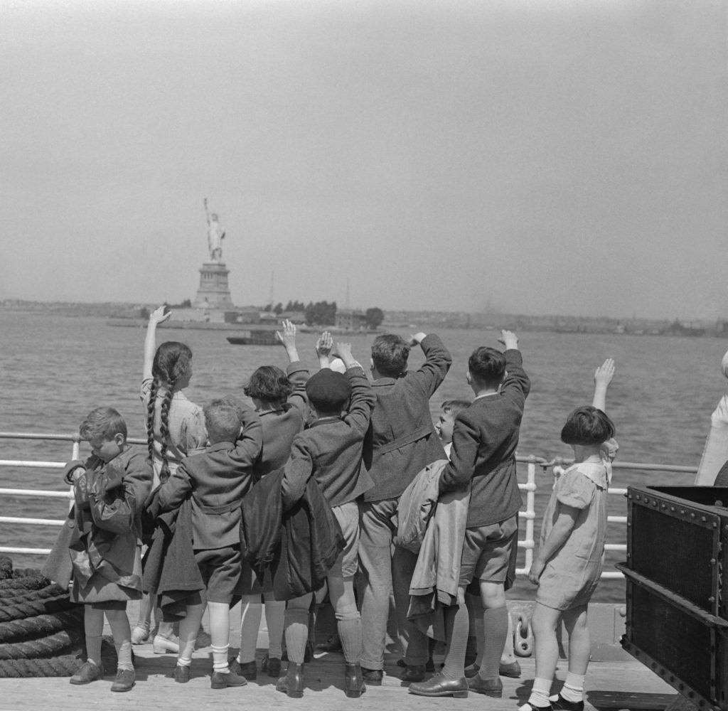 A group of young Austrian immigrants wave to the Statue of Liberty upon their arrival in America aboard the S.S. Harding. The fifty Jewish children, who were greeted by their new adoptive families, were fleeing Nazi persecution in their homeland. Photo by Bettmann/via Getty Images