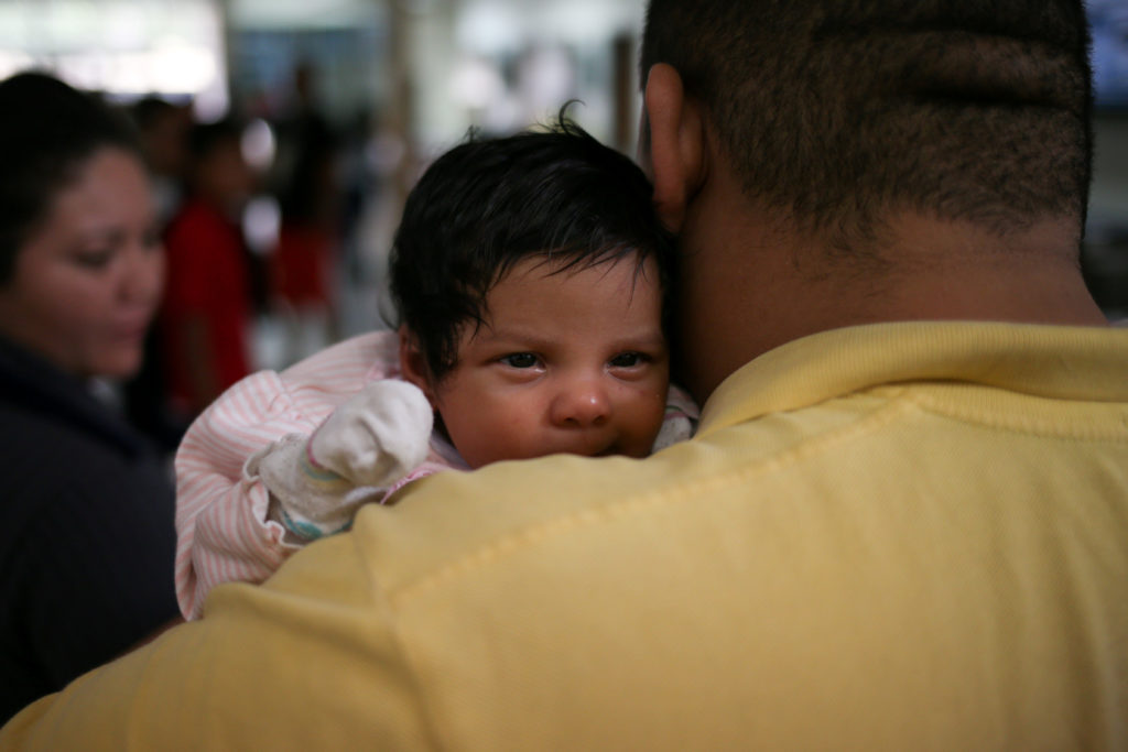 An undocumented immigrant father from Honduras and his infant daughter are released from detention with other families at a bus depot in McAllen, Texas. A study of immigration in Germany found children given citizenship at birth had better health outcomes. Photo by Loren Elliott/Reuters