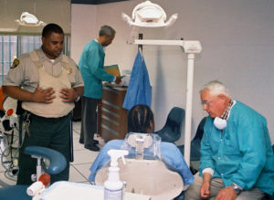 Dentist provides dental care to an inmate as a guard looks on at San Quentin State Prison.