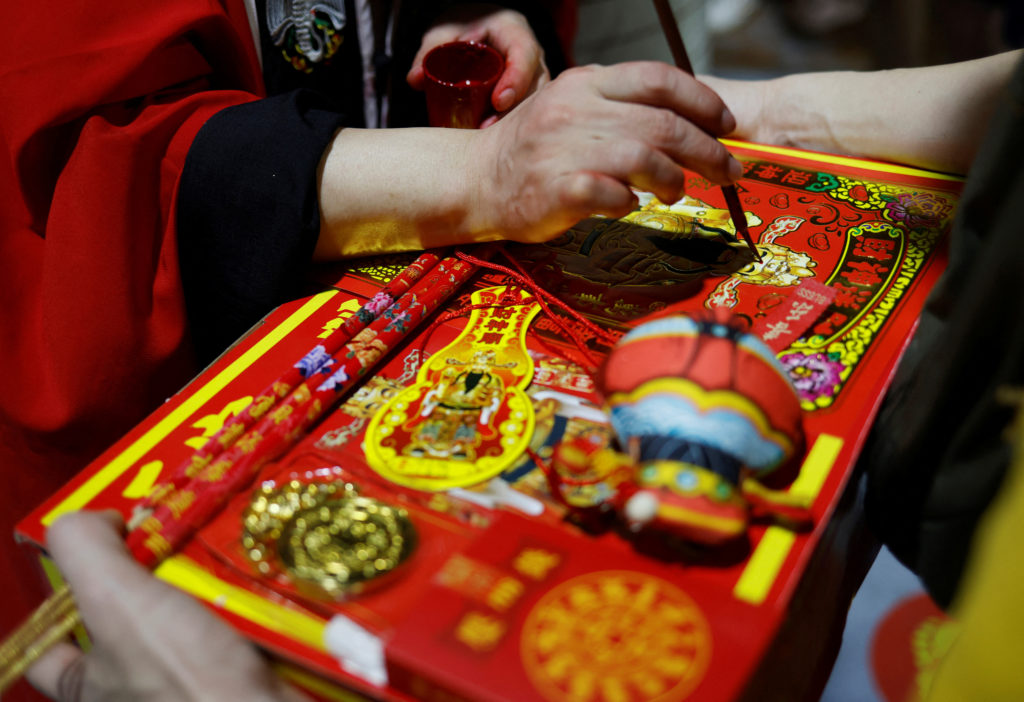 A priestess marks a devotee's offerings during a ceremony to welcome the God of Wealth at a temple on the eve of the Lunar...