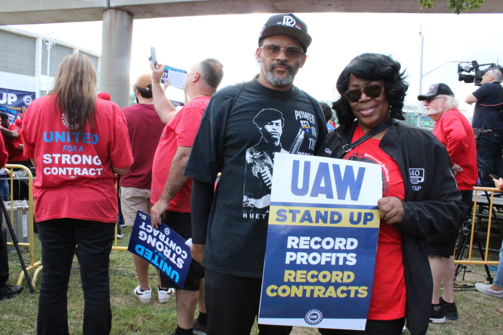 Terance Drake, a member of UAW Local 140 who works at Stellantis’ Warren Truck Assembly Plant, at the UAW’s “Stand up for our Communities against Corporate Greed” rally in Detroit, with a sign that reads, "UAW Stand up record profits record contracts." September 15, 2023. Photo by Frances Kai-Hwa Wang for the PBS NewsHour