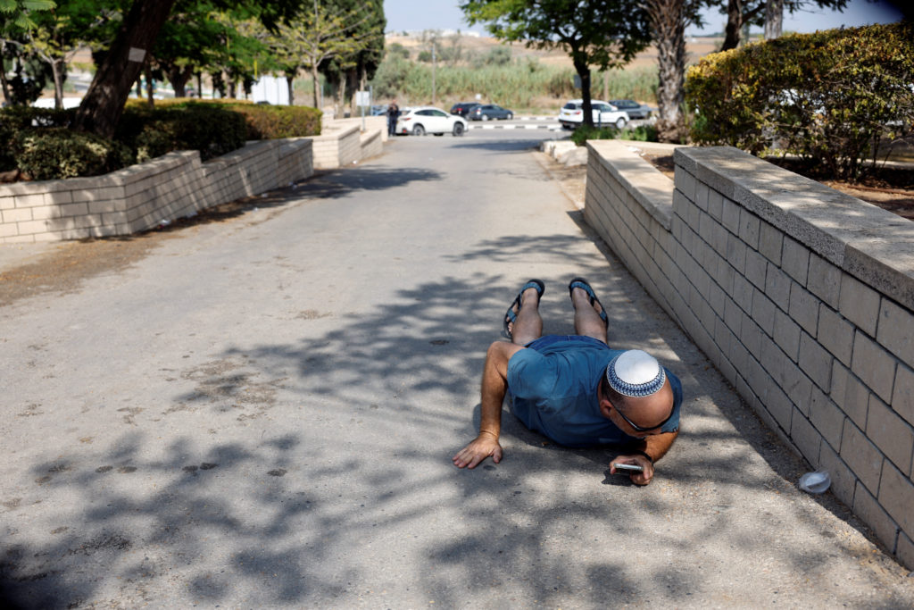A man takes cover while sirens sound as rockets from Gaza are launched towards Israel, in Ashkelon, southern Israel