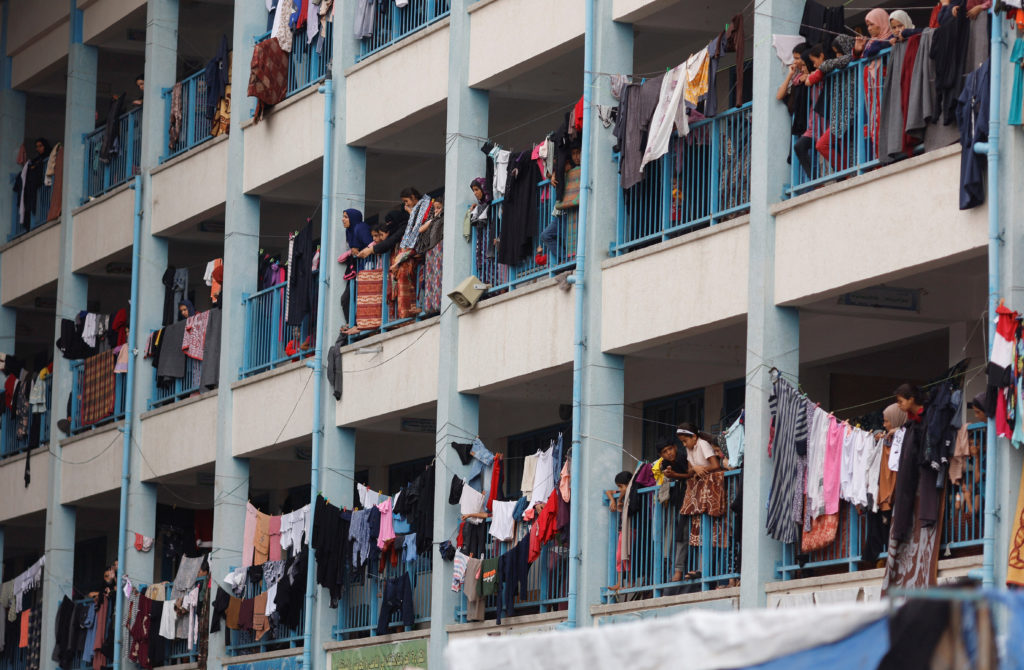 Palestinians, who have fled their homes due to Israeli strikes, watch a nearby Israeli strike as they take shelter in a UN...