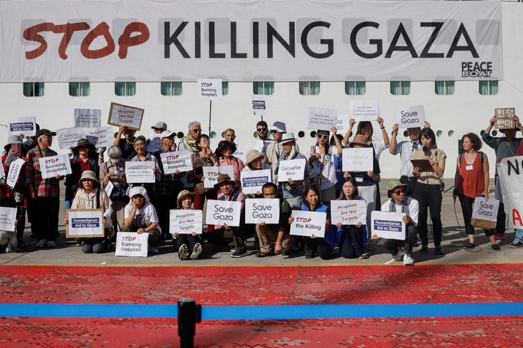 People hold placards in front of Japan-based NGO Peace Boat in the port of Piraeus, Greece, November 3, 2023. The cruise ship starts a global cruise calling for a ceasefire in Gaza, at the port, where it will dock its cruise ship and hold a protest, before travelling to 20 other ports around the world as part of the initiative. Photo by Louisa Gouliamaki/REUTERS