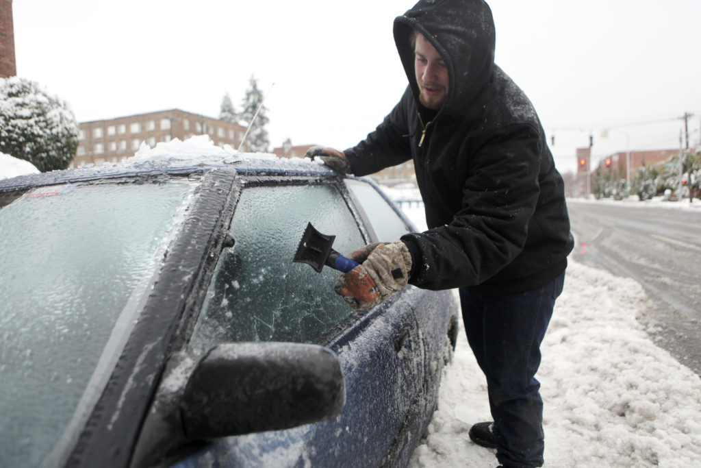 Chris Monson, a local resident, breaks ice off his car with an ice scraper in Tacoma, Washington