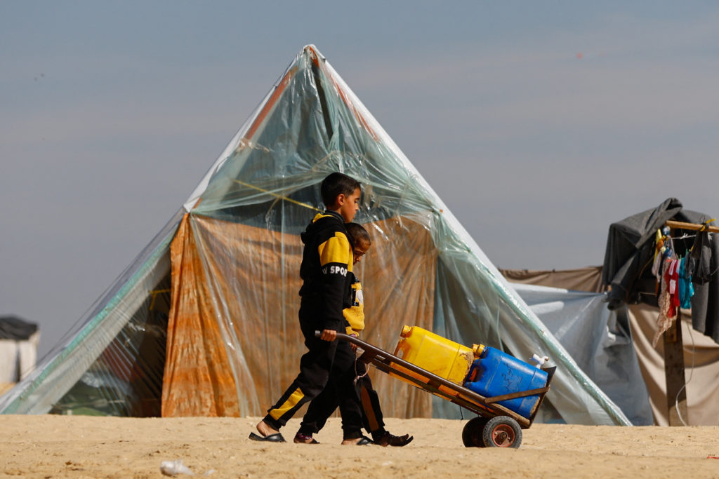 Boys transport containers on a hand trolley, as displaced Palestinians, who fled their houses due to Israeli strikes, take shelter in a tent camp, amid the ongoing conflict between Israel and the Palestinian Islamist group Hamas, at the border with Egypt, in Rafah in the southern Gaza Strip, February 8, 2024. Photo by Ibraheem Abu Mustafa/Reuters