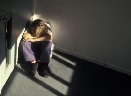 Young boy sitting in dark corner of stairs. Victim of child abuse