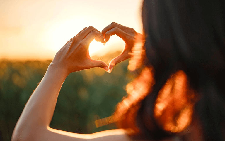 Girl looking at the sunset and showing heart symbol with her hands
