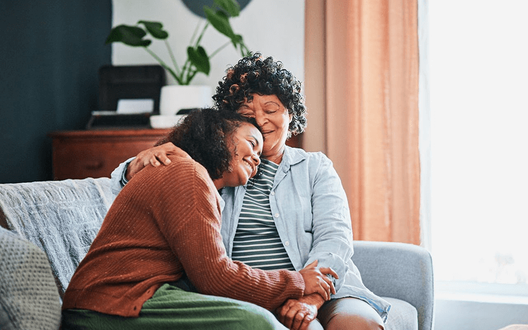Mother hugging her daughter while sitting on a  couch