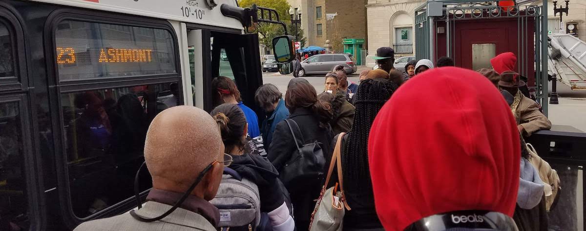 A large crowd of people stand outside a 23 bus to Ashmont, waiting to board.