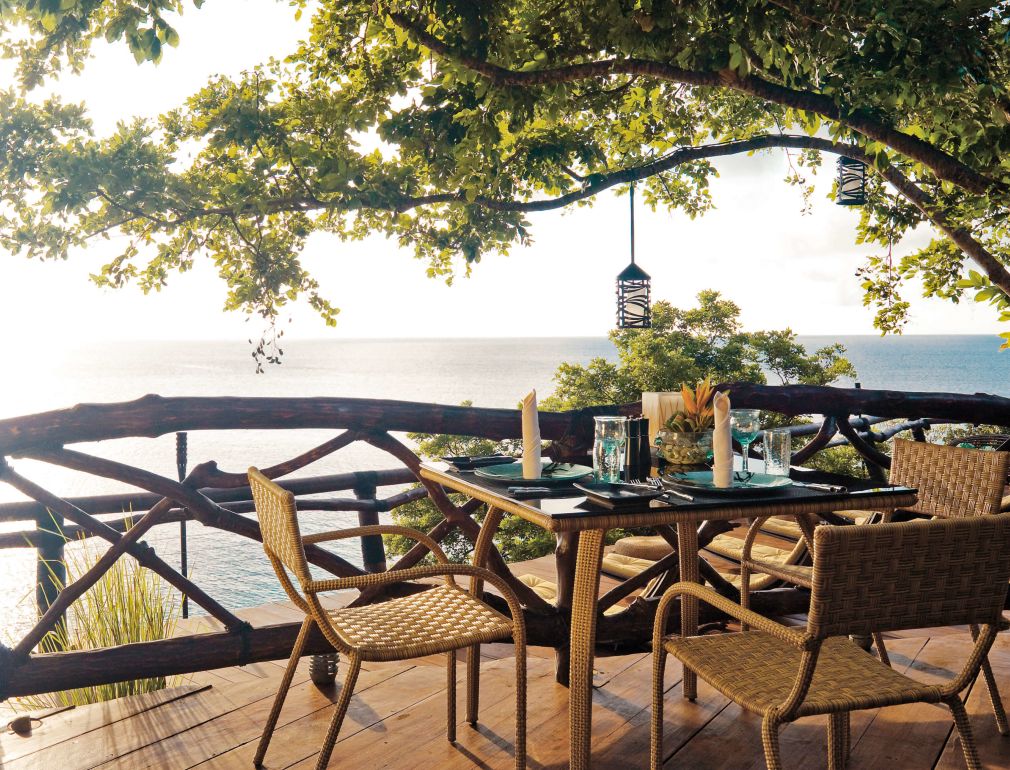 A Table Set With Chairs And A Tree With A Body Of Water In The Background