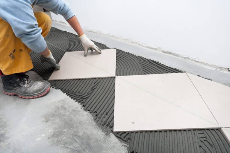 Worker laying white tile on concrete.