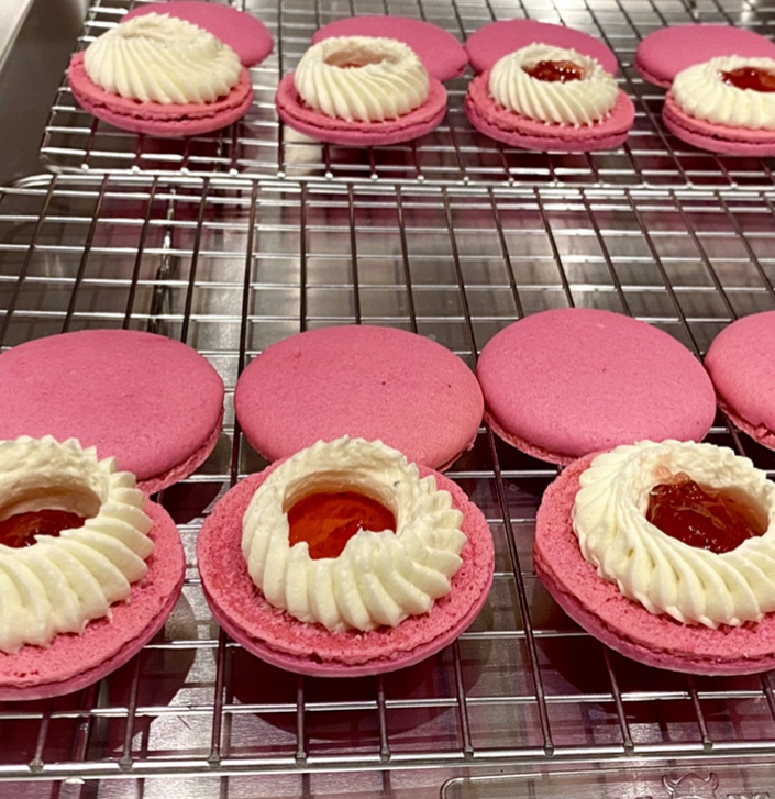 macaron shells filled with merignue and fruit filling on a cooling rack on counter