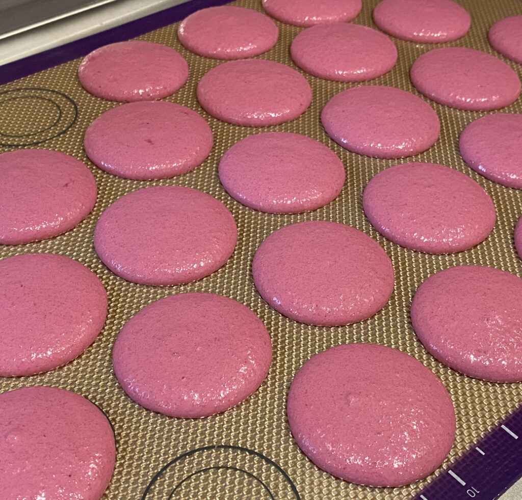 piped macaron shells on a silicone baking mat 
