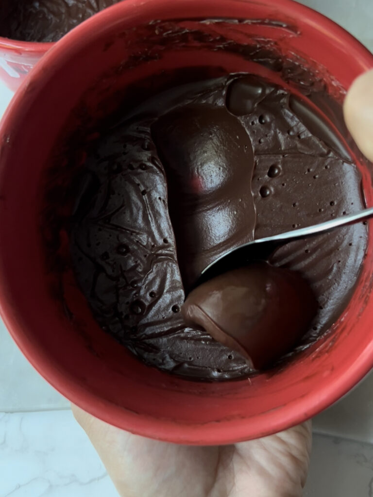 thickened chocolate ganache in a red bowl with a spoon in it 