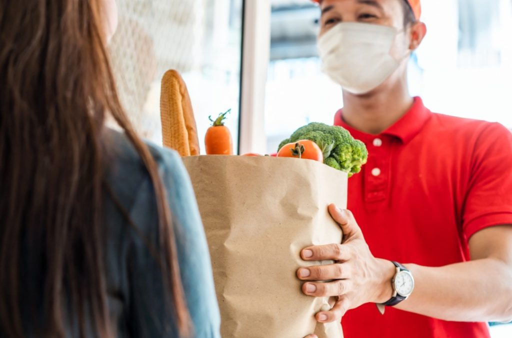 entregador usando máscara de proteção entregando as compras em casa a uma cliente