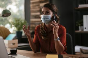 Linda mulher de negócios com máscara médica, trabalhando no escritório. Jovem empresária falando ao telefone. Mudança de comportamento das pessoas.