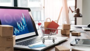 Sacos de compras no carrinho de compras e cartão de crédito no laptop com caixas de papel na mesa e gráfico de crescimento econômico de dados de vendas na tela, serviços de compra e venda online na rede, compras online e conceito de e-commerce. Tendências de inovação no setor do varejo.