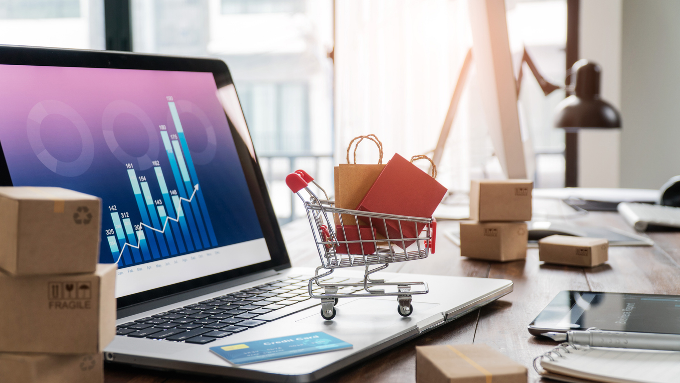 Sacolas de compras no carrinho de compras e cartão de crédito no laptop com caixas de papel na tabela e gráfico de crescimento econômico de dados de vendas na tela, compra e venda de serviços on-line na rede, compras on-line e conceito de comércio eletrônico.