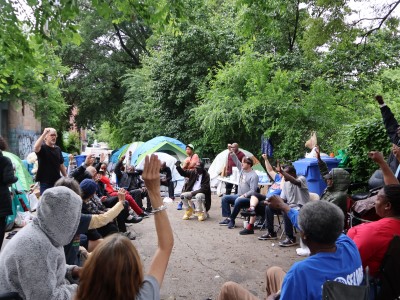 A group of people sitting in a circle on a gravel backstreet discussing housing first policy for Atlanta.