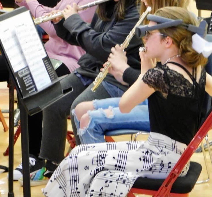 Rhylee reading a sheet of music with her eSight 4 while playing the flute.