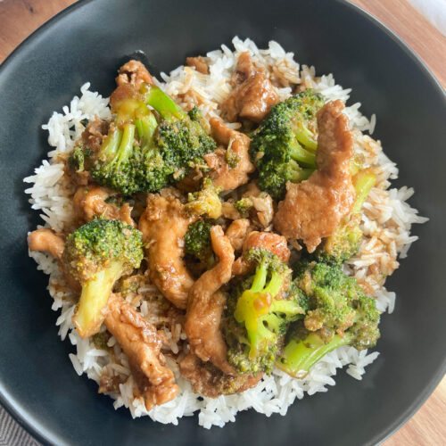 Chicken and broccoli stir-fry served oven white rice in a black bowl.