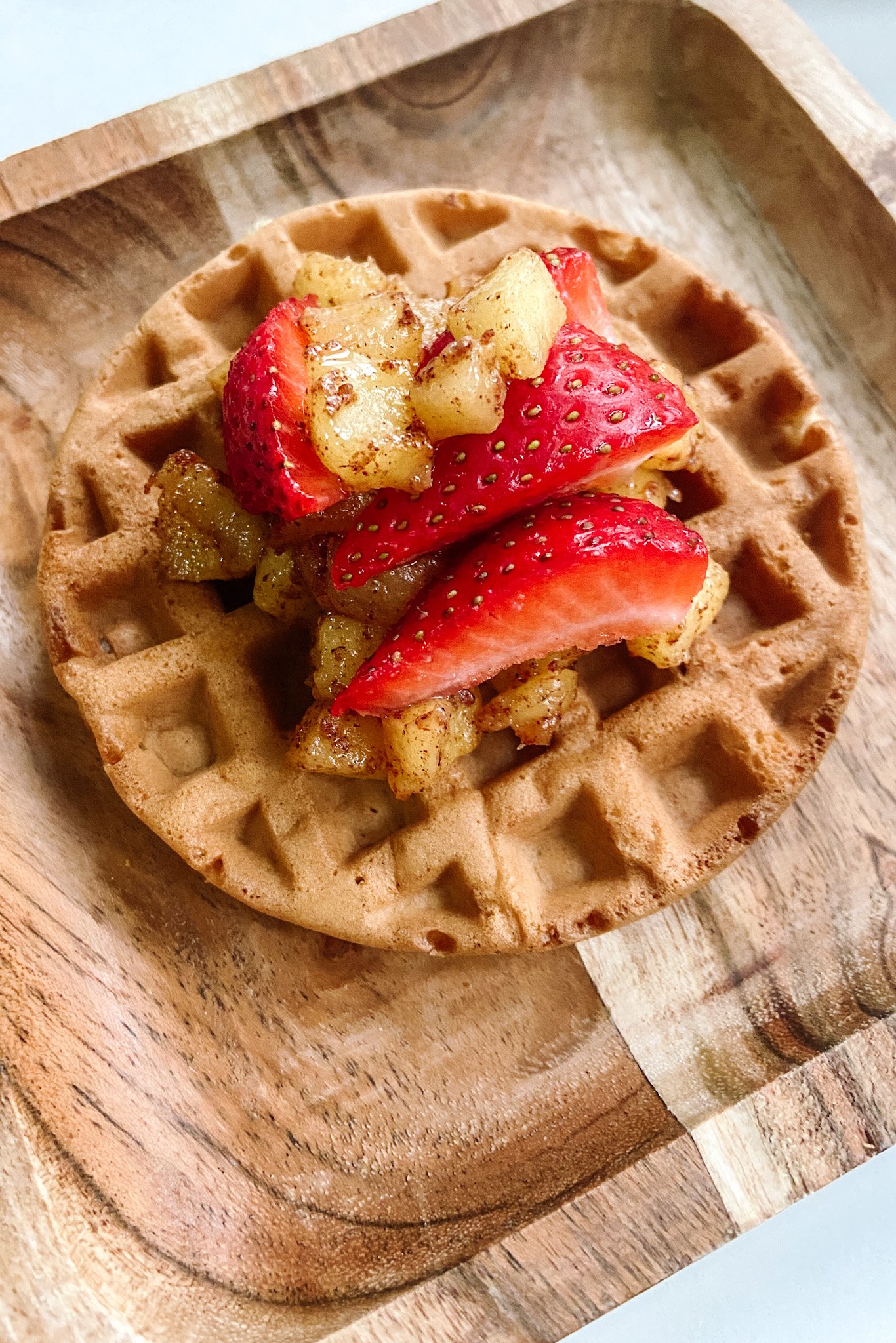 Cinnamon apple waffle topped with cinnamon apples and sliced strawberries.