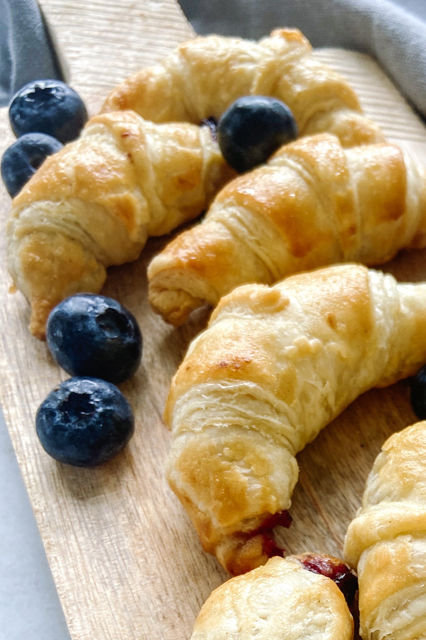 Mini blueberry croissants served on a wooden cutting board with blueberries