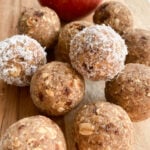 Apple pie bliss balls served on a wooden cutting board. Fuji apple shown in the background