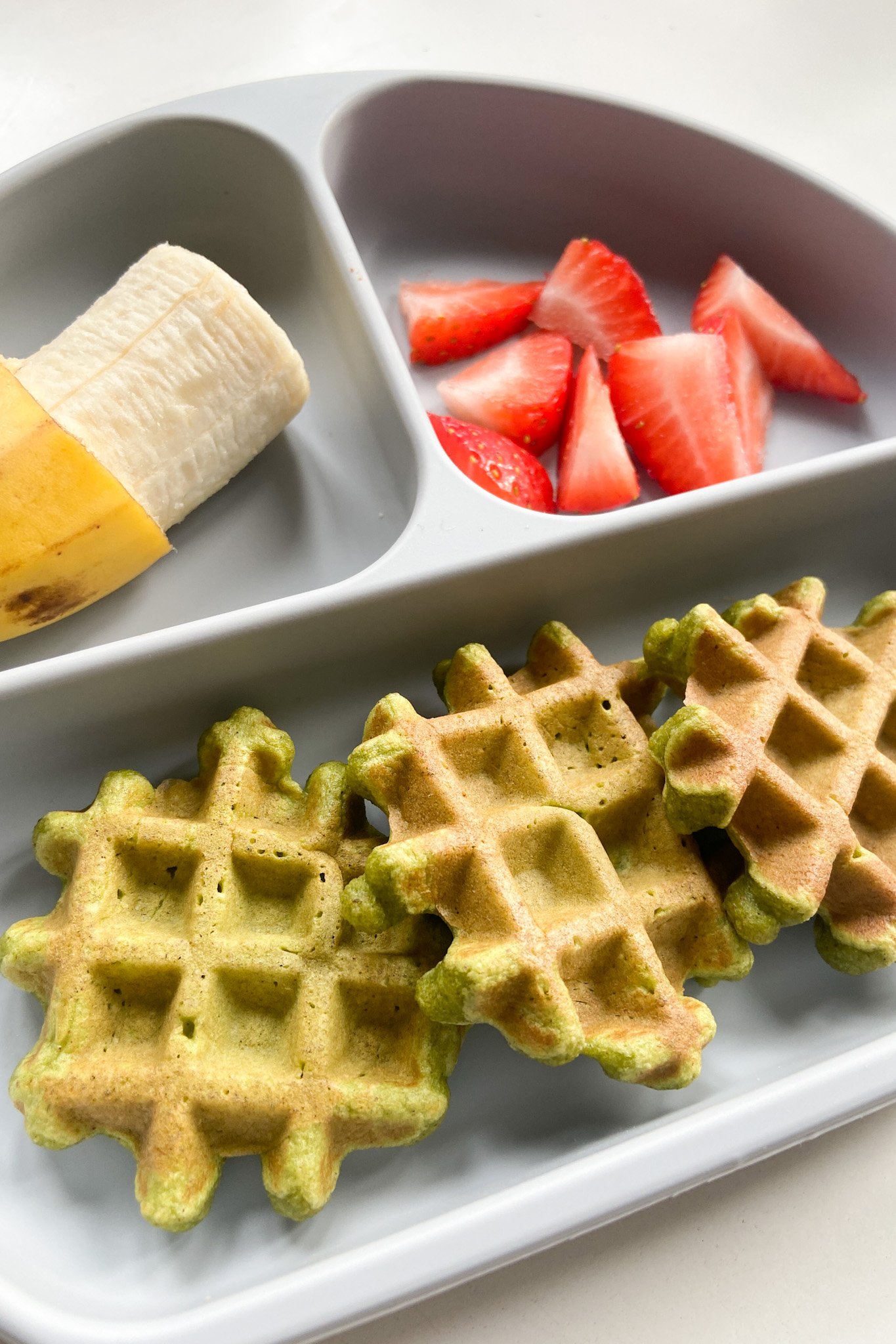 Spinach banana waffles served with a banana and strawberries