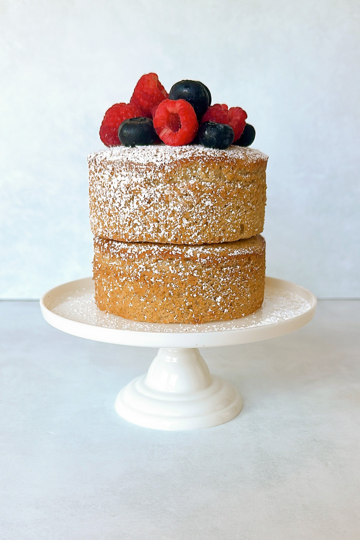Apple almond cake on a cake stand topped with fresh berries.