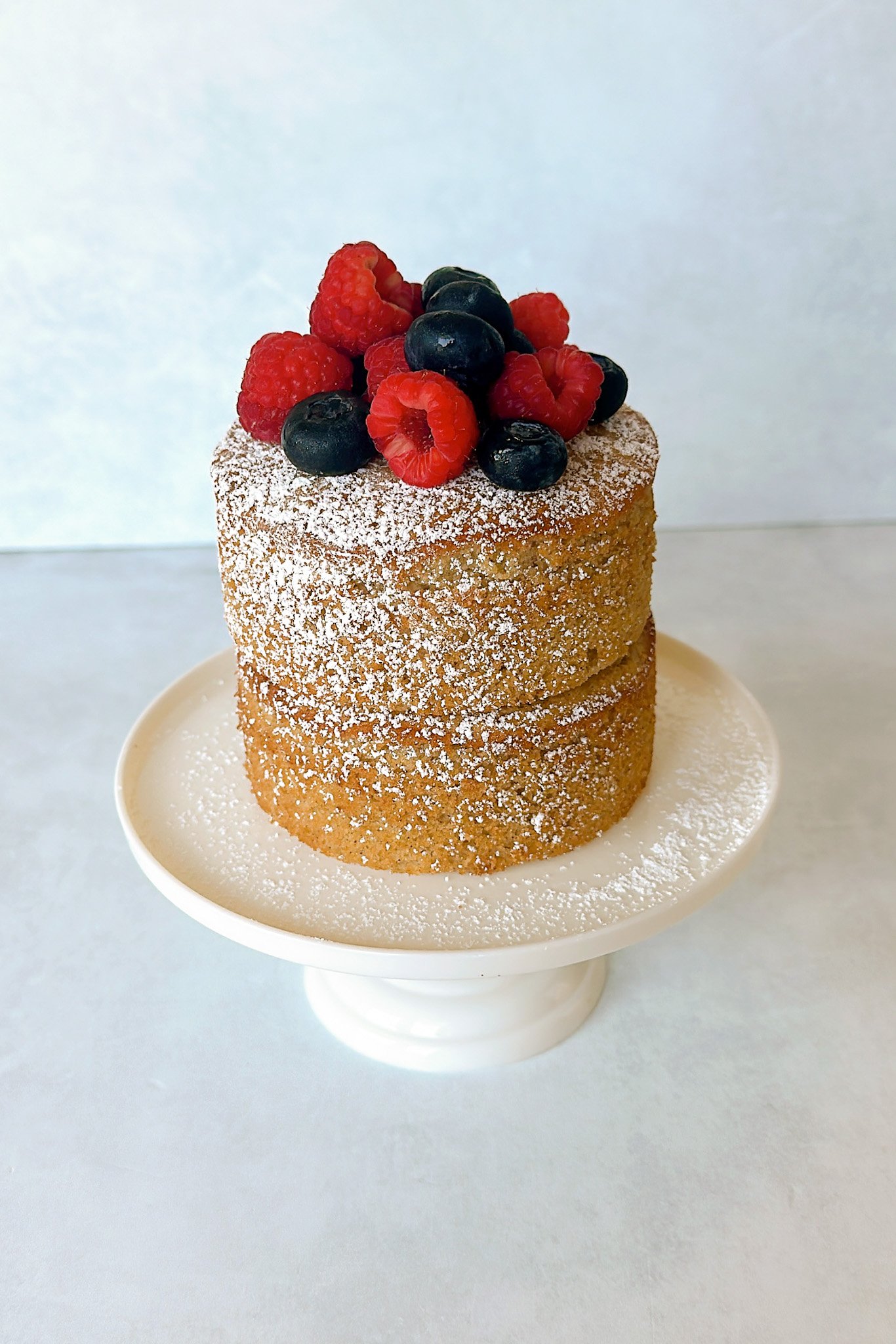 Apple almond cake on a cake stand topped with fresh berries.