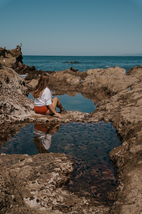 a woman sitting beside tidepools in santa teresa beach costa rica