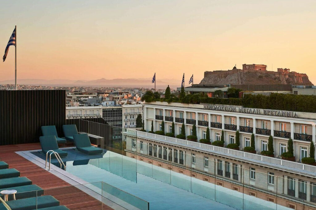 Sleek Athens hotel with pool on the roof at dusk with white building and Acropolis in front