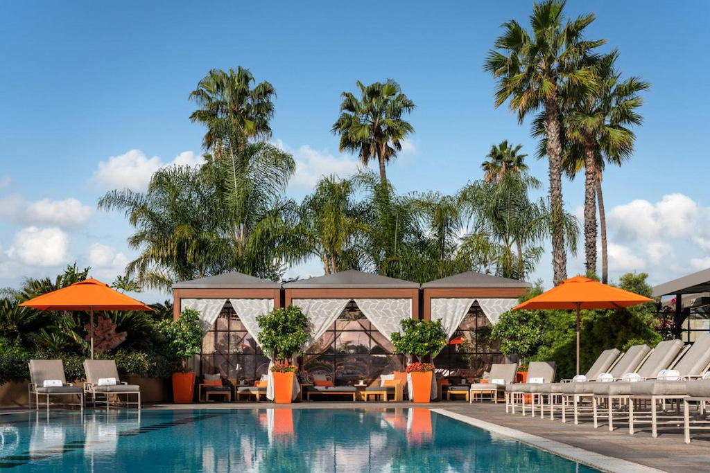 Luxury hotel in Beverly Hills with pool, sunbeds and orange umbrellas with palm trees in the background