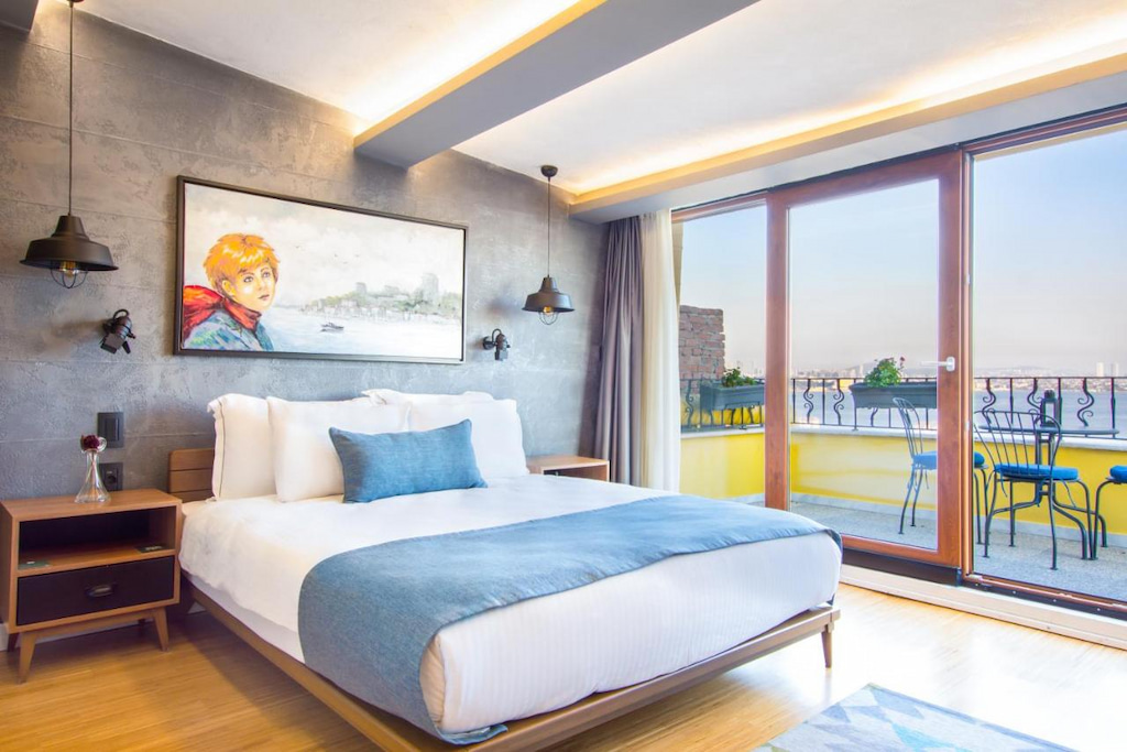 light and bright hotel in Istanbul with large bed with white and blue linens, expansive floor to ceiling windows with balcony and grey feature wall