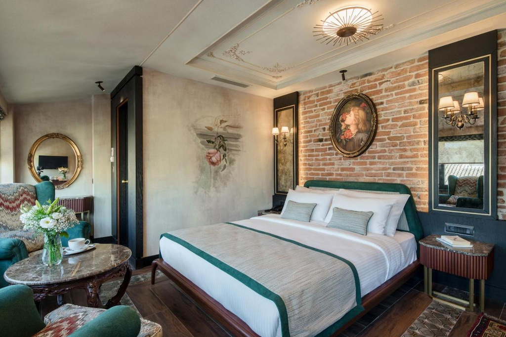 traditional Turkish interior design adorn this best boutique hotel in Istanbul with large bed with white and green linens, brick wall and resting table
