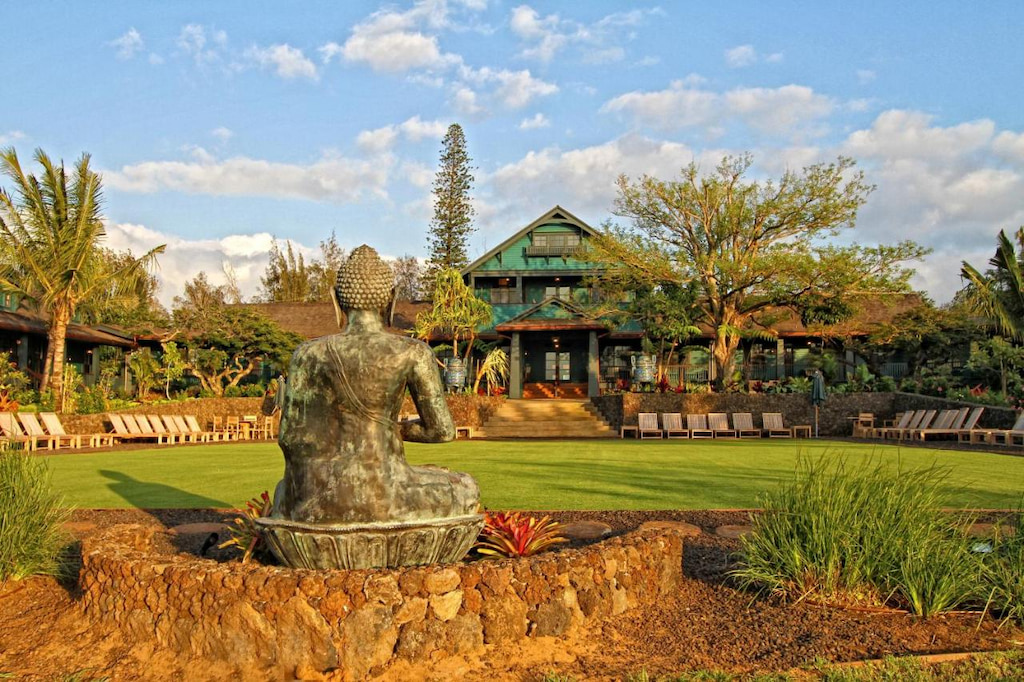 A green statue located in the middle of the front yard of Lumeria Maui Hotel with green paint surrounded by white benches