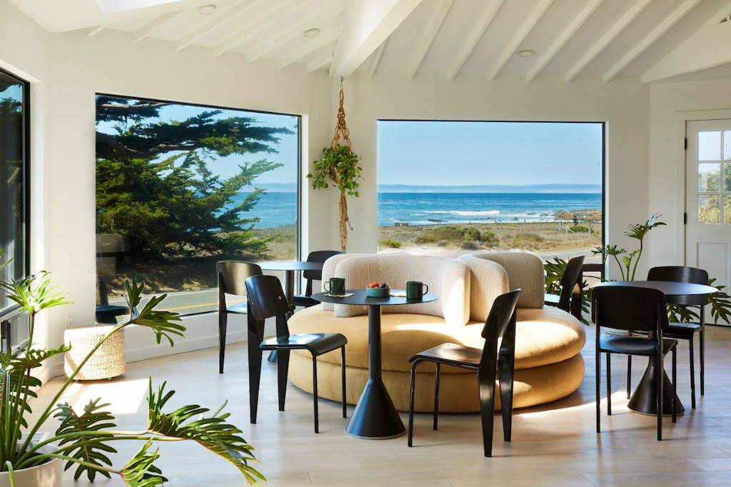 The lounge of the White Water with black tables and chairs with the beautiful view of the sea and beach through large windows.