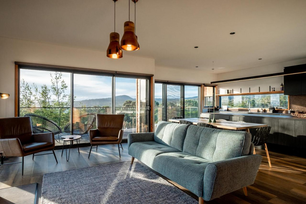 comfortable blue couch and chairs with a modern kitchen and floor to ceiling windows in an accommodation Freycinet Tasmania