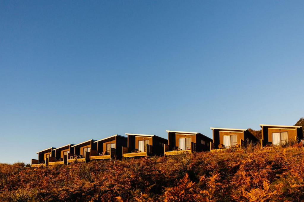 small modern wood cabins with slanted roofs on a hill in Freycinet National Park at golden hour