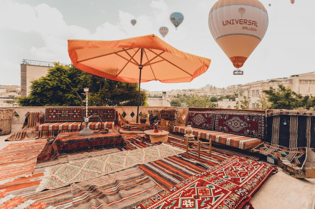 hotel in Cappadocia with best view of the hot air balloons in the background and orange umbrella and multi coloured turkish rugs in the foreground