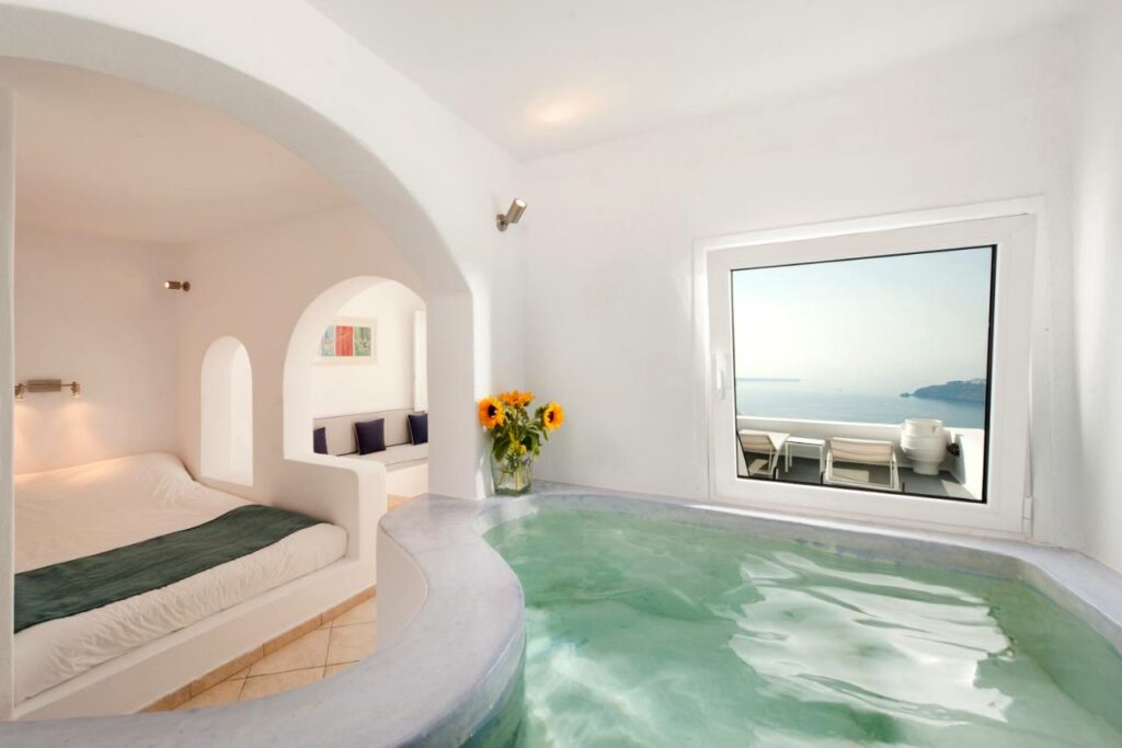 An indoor pool in front of a cozy bed in Regina Mare with sunflowers on a vase in the corner