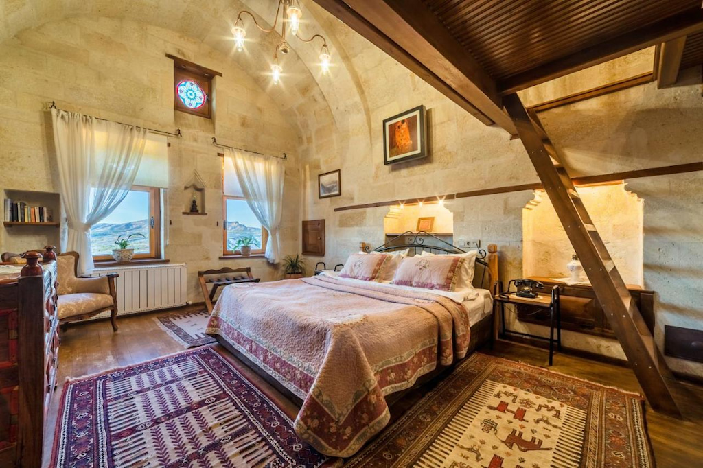 large stone room in luxury Cappadocia hotel room with cozy linen, windows and wood ladder leading up to a loft