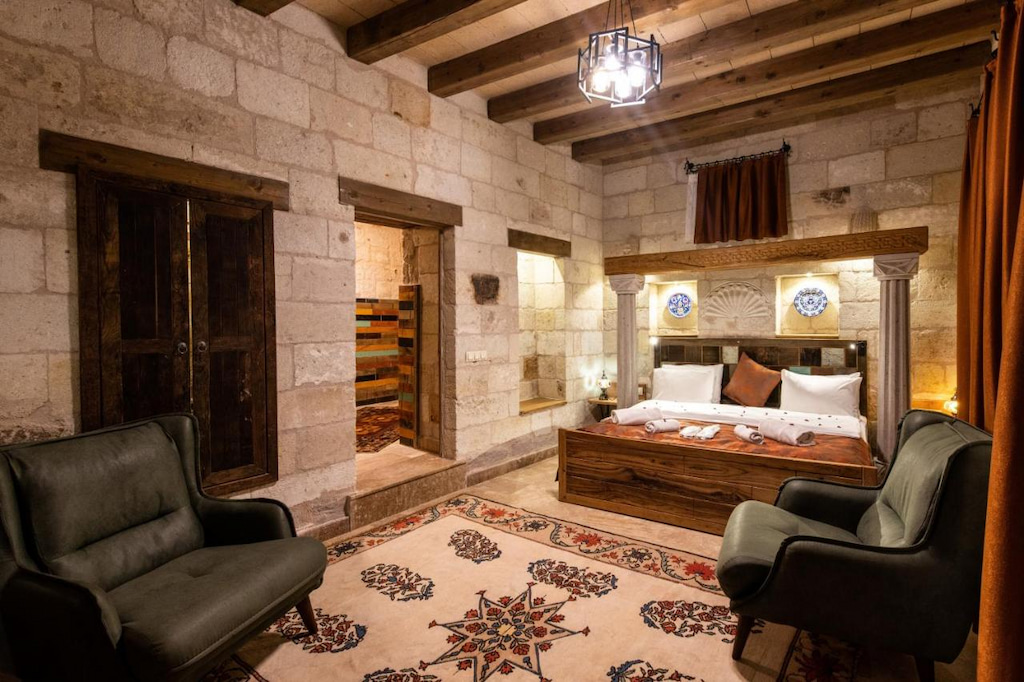 cozy Cappadocia luxury hotel room with wood framed bed, 2 grey lounge chairs and small chandelier